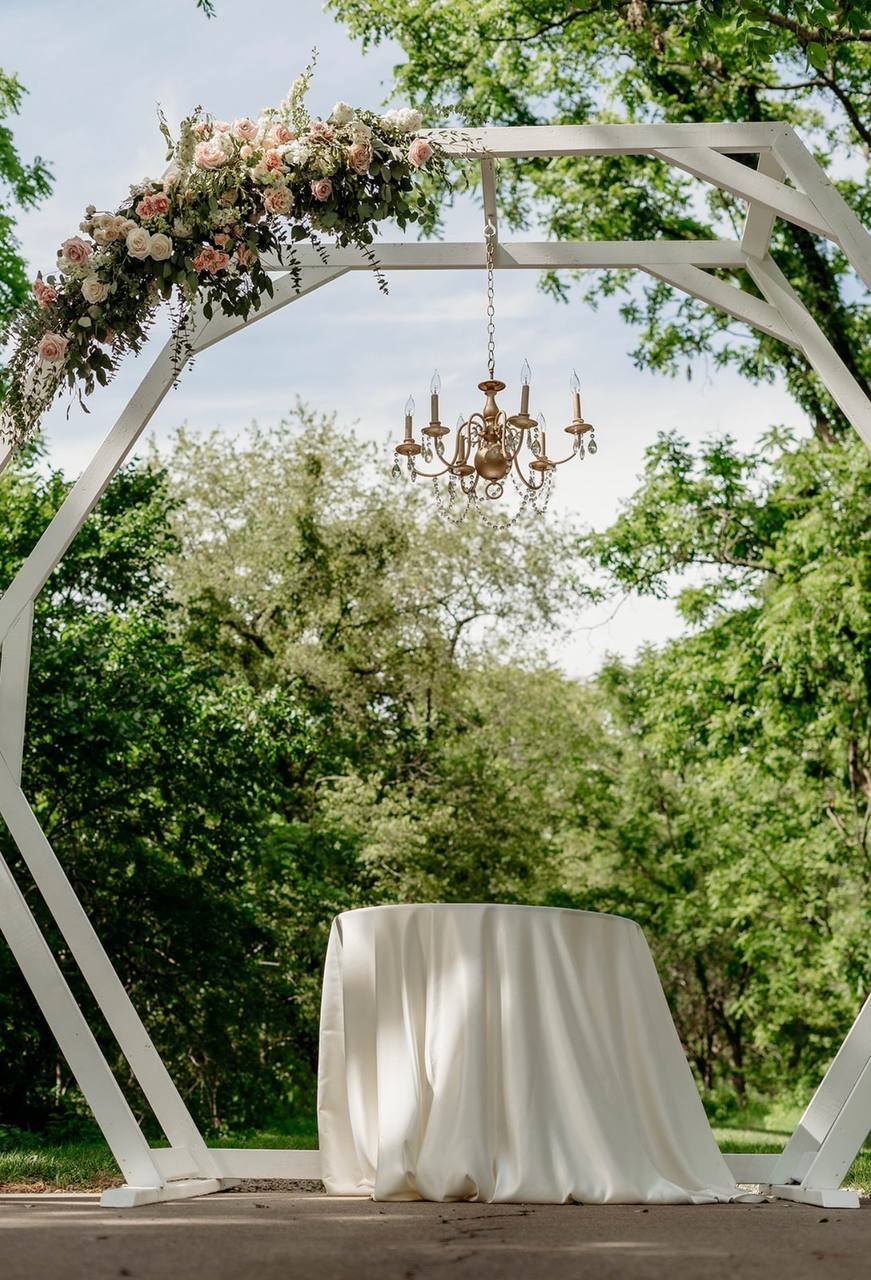 White hexagon arbor with blush roses and a hanging brass chandelier