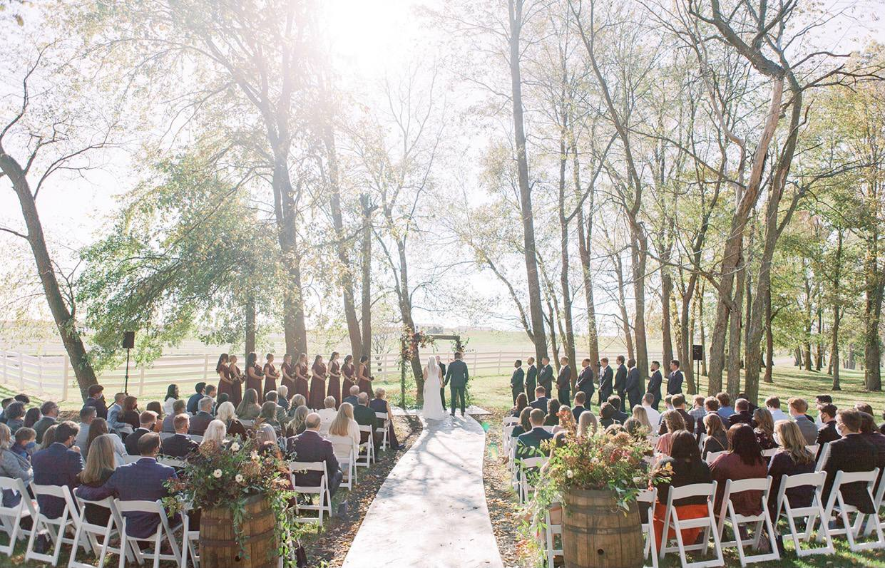 Sunlit autumn ceremony in the tree grove with guests and barrel florals