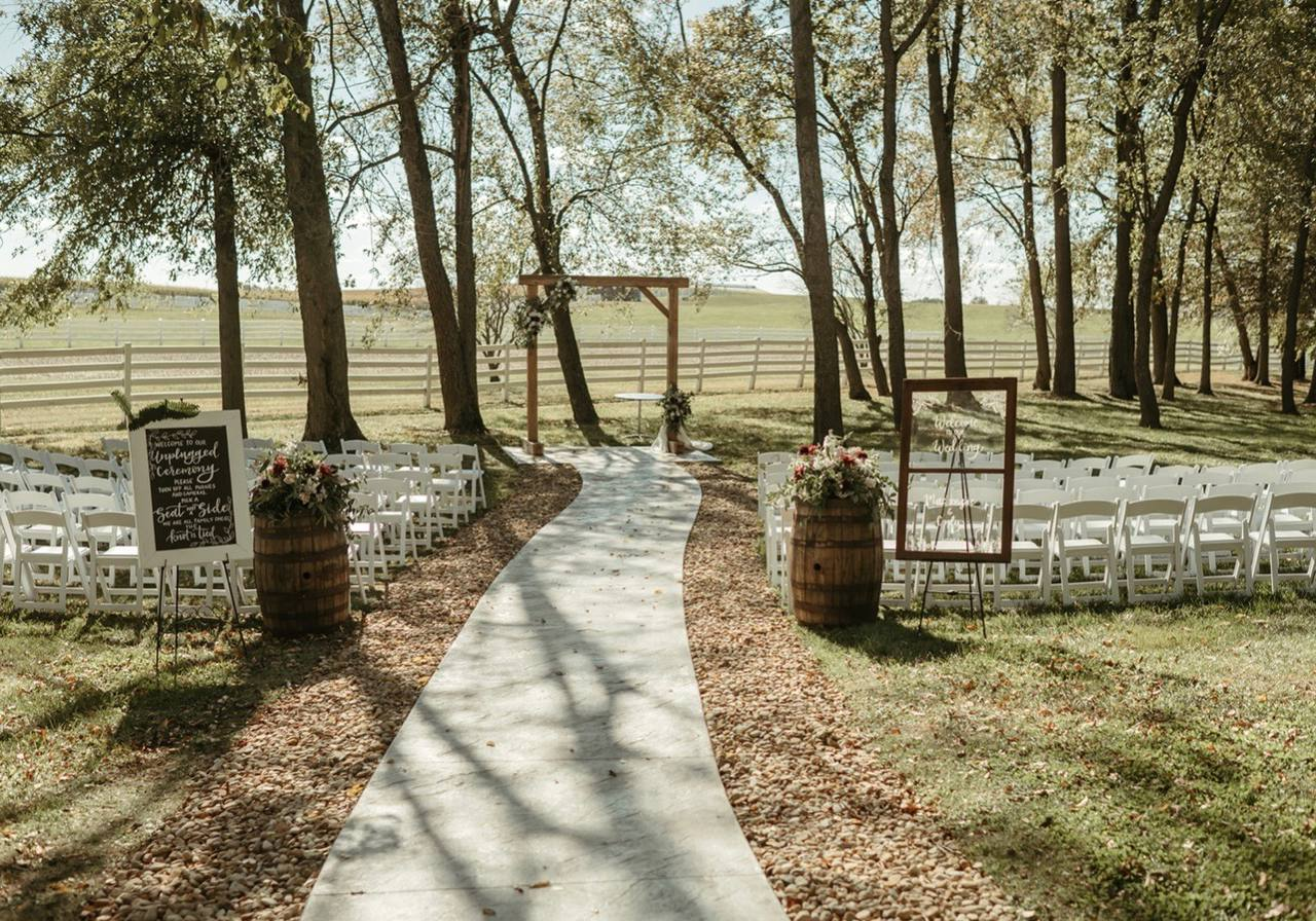 Ceremony aisle beneath the tree grove with welcome signs and barrel florals