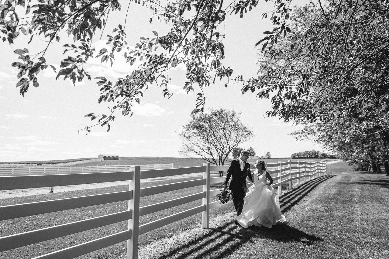 Black and white portrait of the couple walking along the white paddock fencing