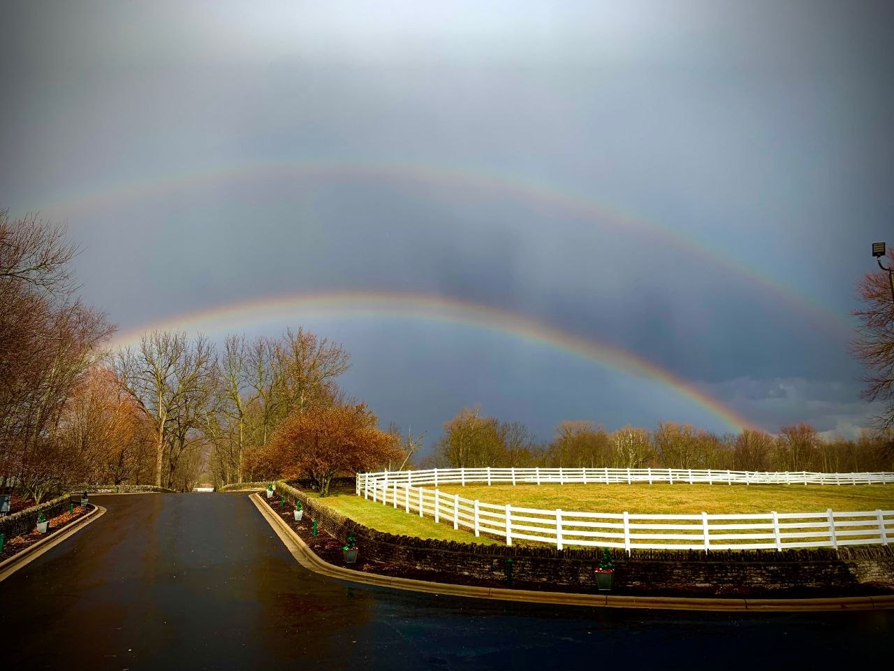 Double rainbow arching over the estate drive and white fencing