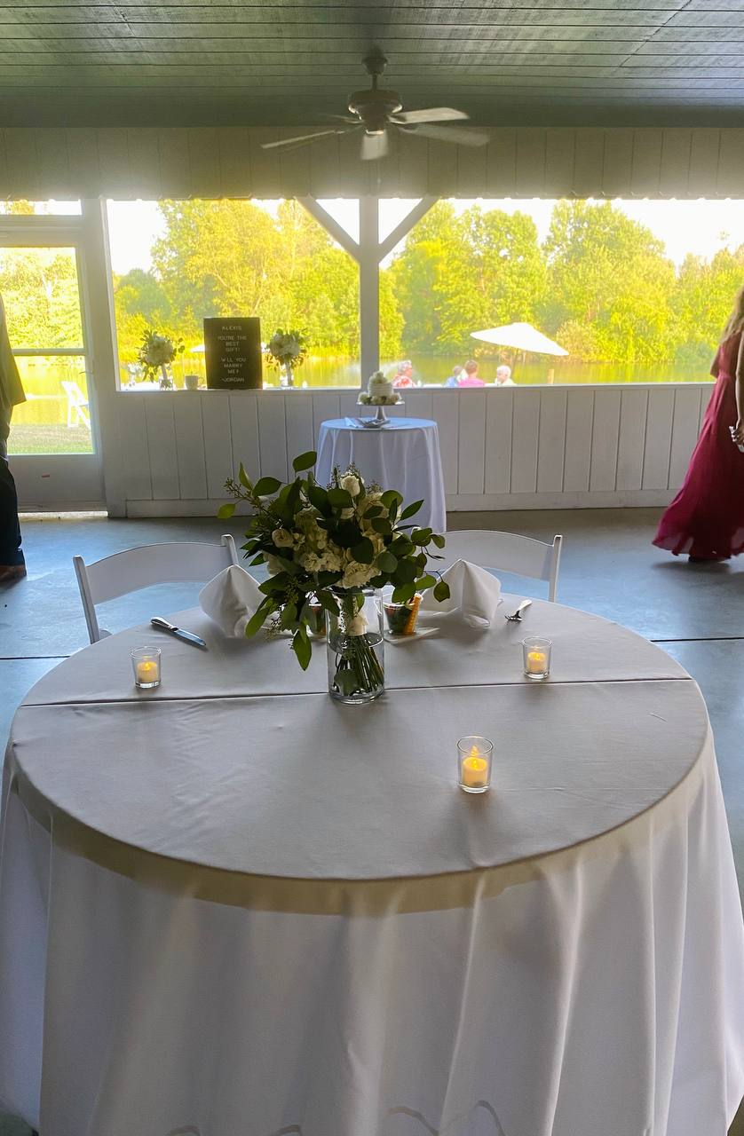 Sweetheart table with candles and white florals on the screened lake house porch