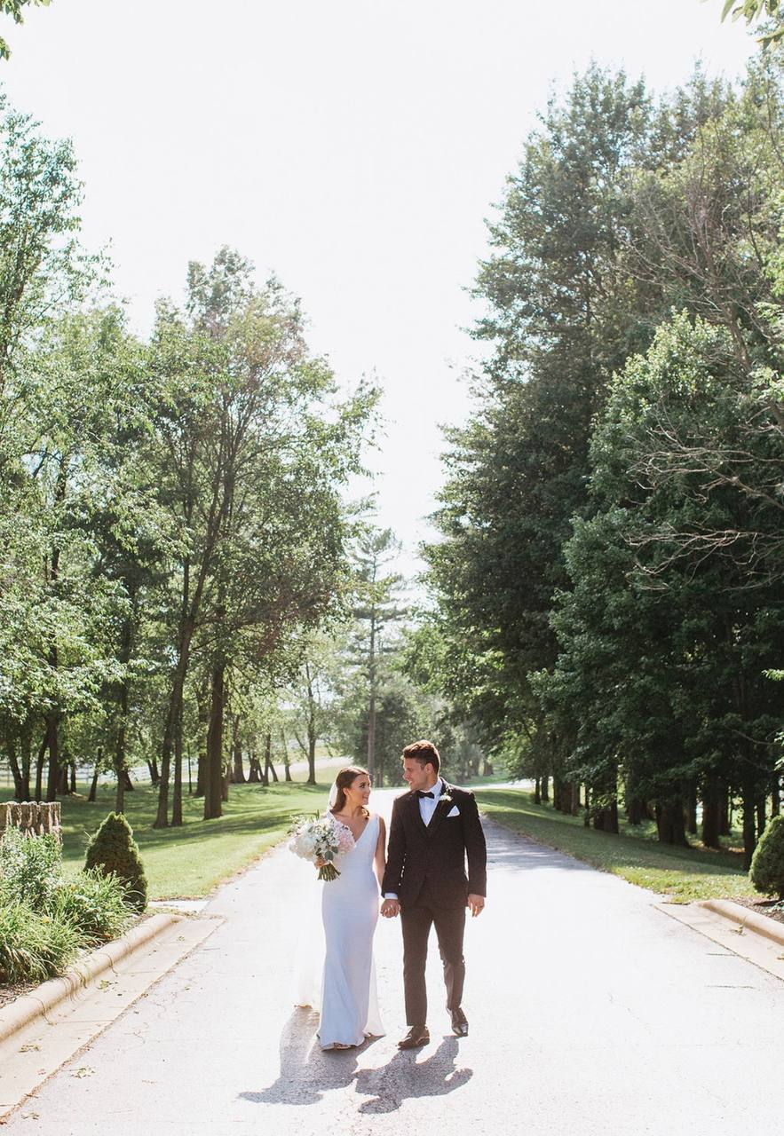 Couple walking hand in hand down the tree-lined estate drive