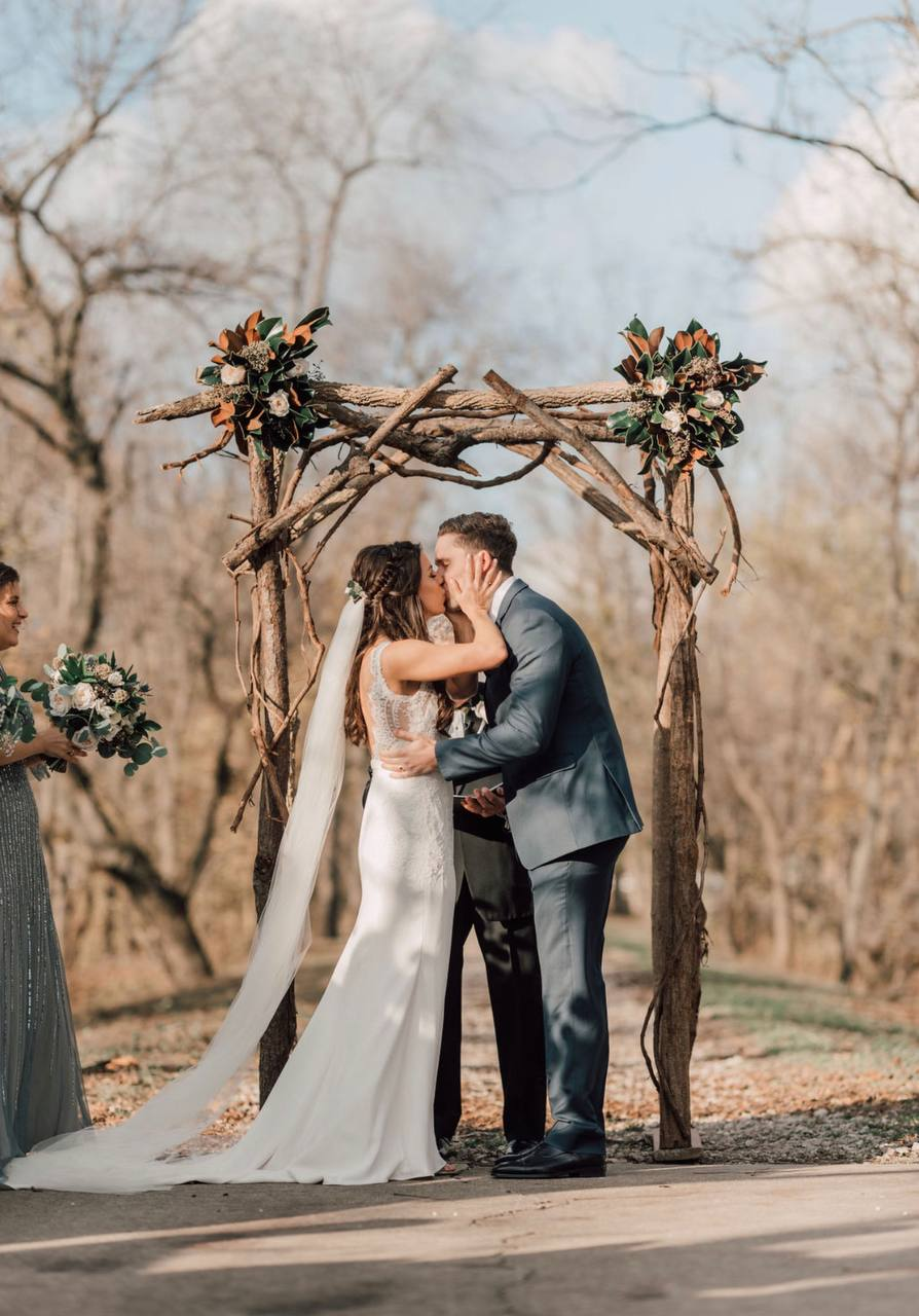 Couple's first kiss beneath a rustic branch arbor with magnolia accents