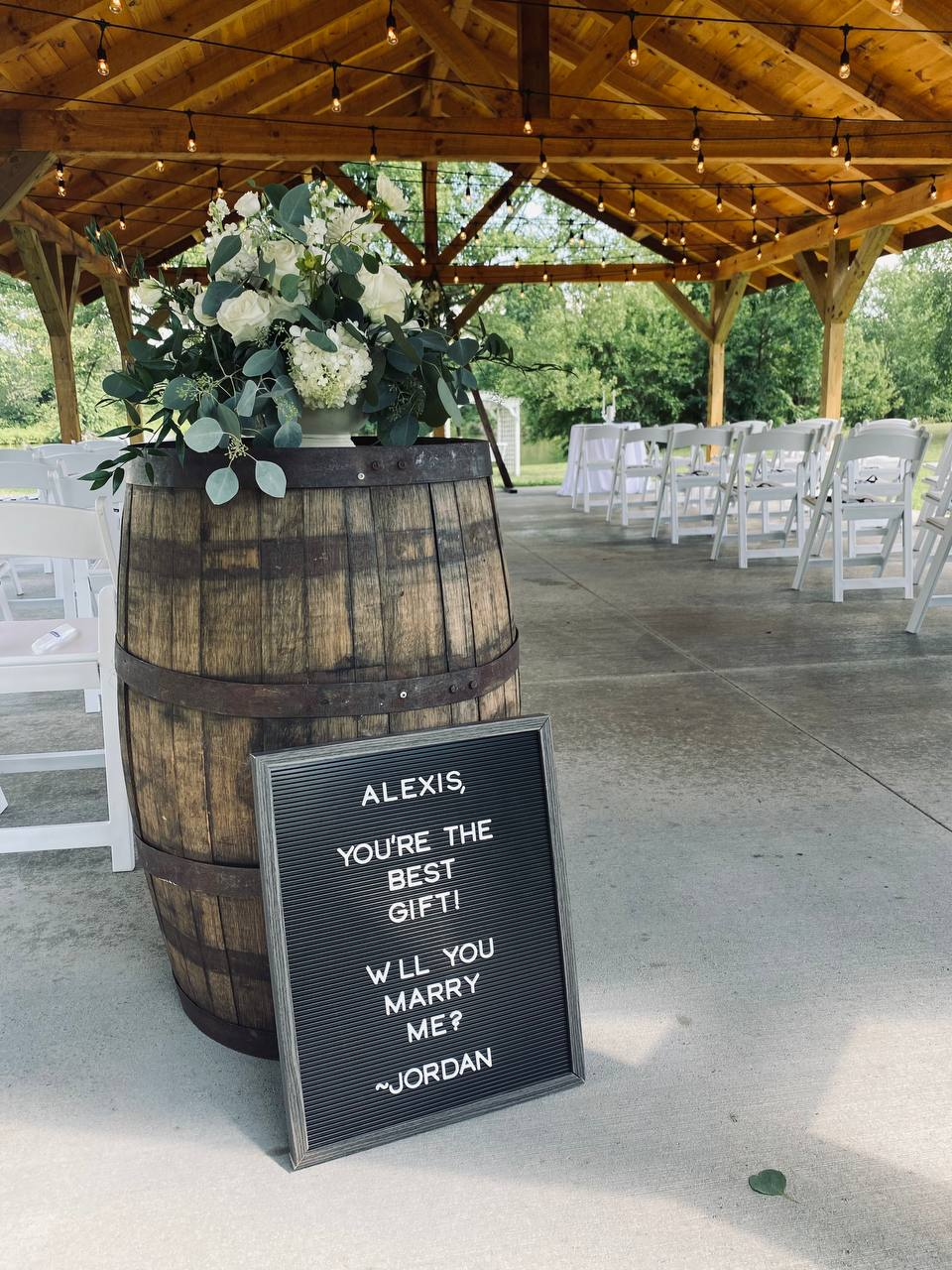 Letterboard proposal sign beside a whiskey barrel of white florals in the pavilion