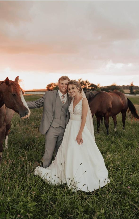Bride and groom in the pasture at sunset as horses graze behind them