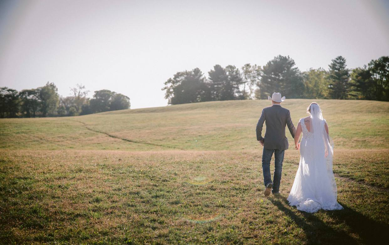 Couple walking across the open meadow toward the tree line at golden hour