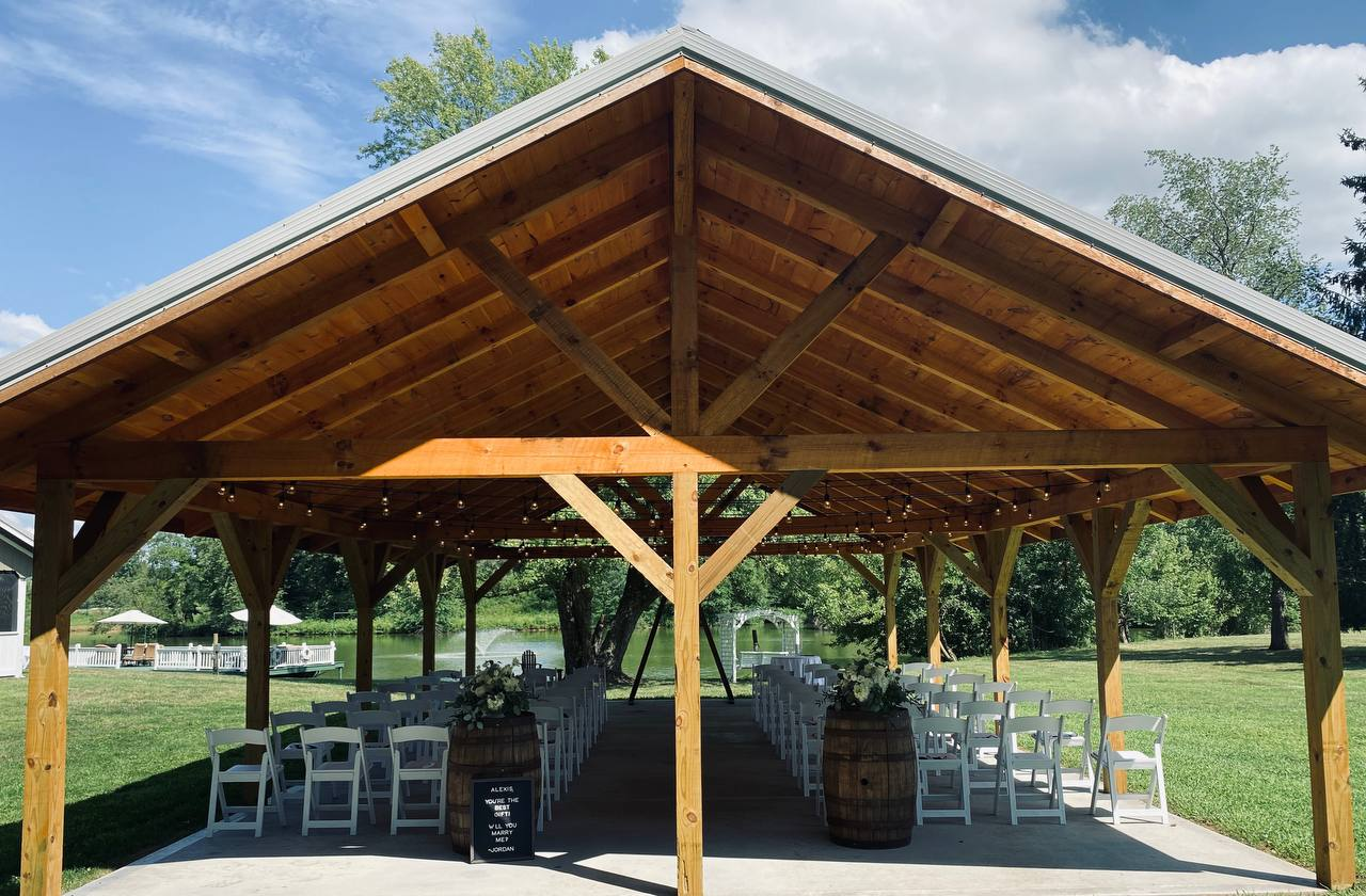 Timber-frame pavilion set with white chairs for a lakeside ceremony