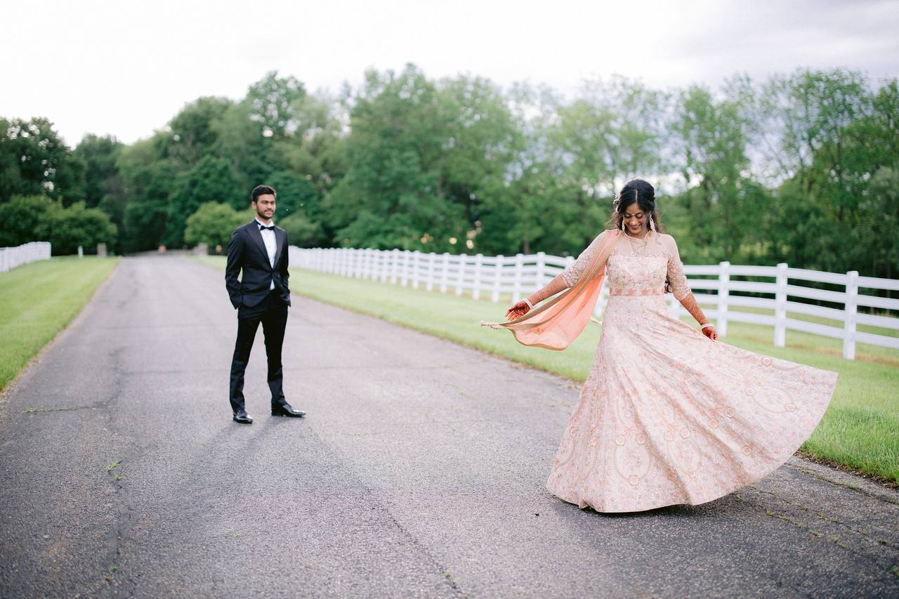 Bride twirling in a blush lehenga on the estate drive with the groom looking on