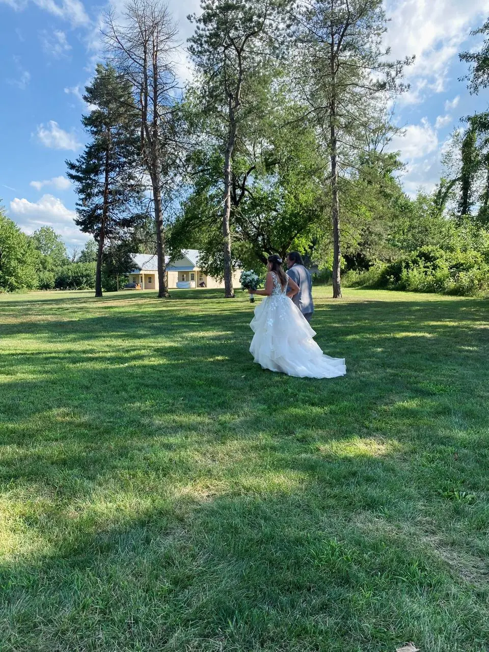Bride and groom walking across the estate lawn beneath tall pines